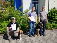 Zwei Hundeführer mit Hunden und eine Begleitperson mit Urkunden für M-Prüfung.